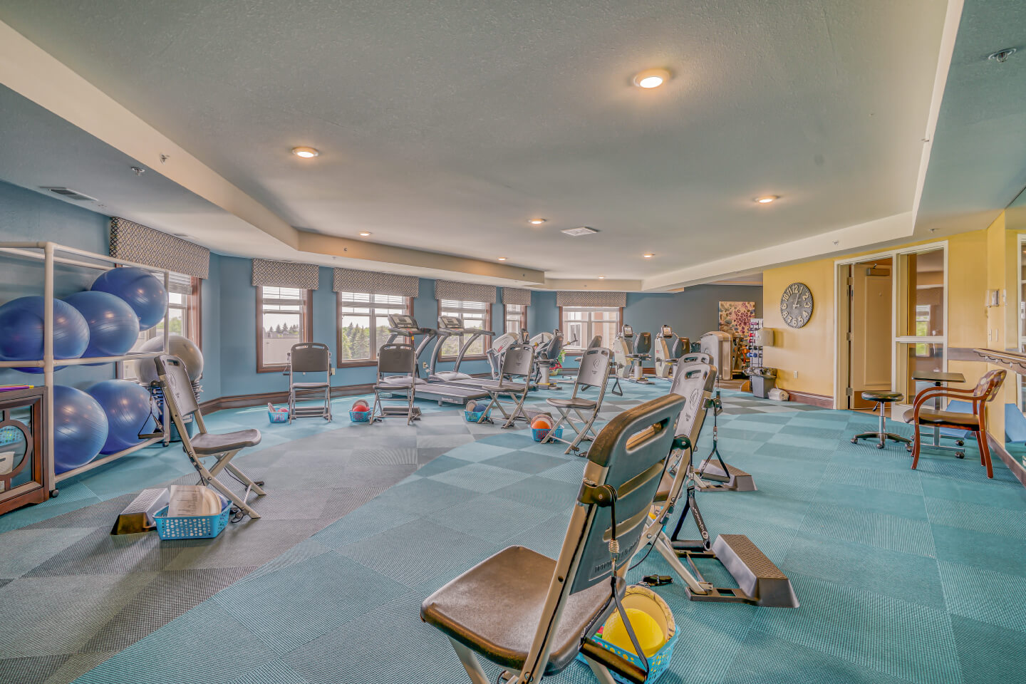 Spacious gym with exercise equipment, chairs, and stability balls in a senior living community.