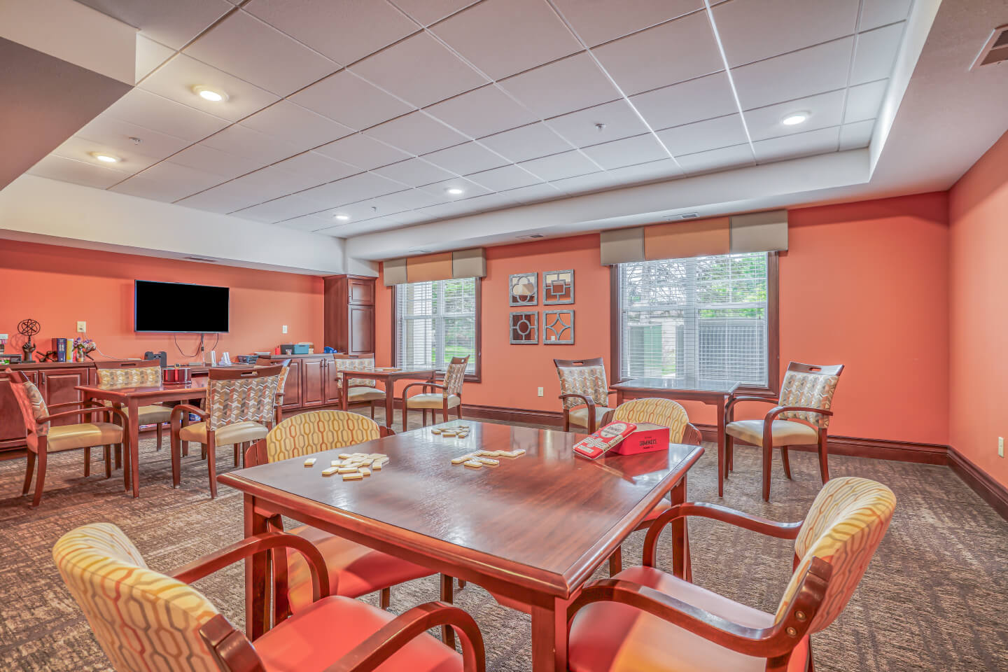 Community game room with tables, chairs, a TV, and large windows at a senior living community.