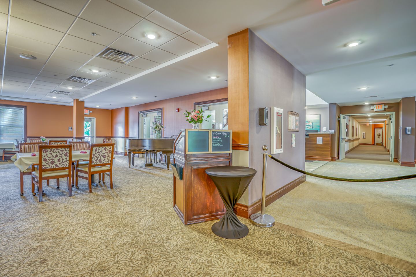 Spacious lobby and dining area in a senior living community with tables, chairs, and a piano.