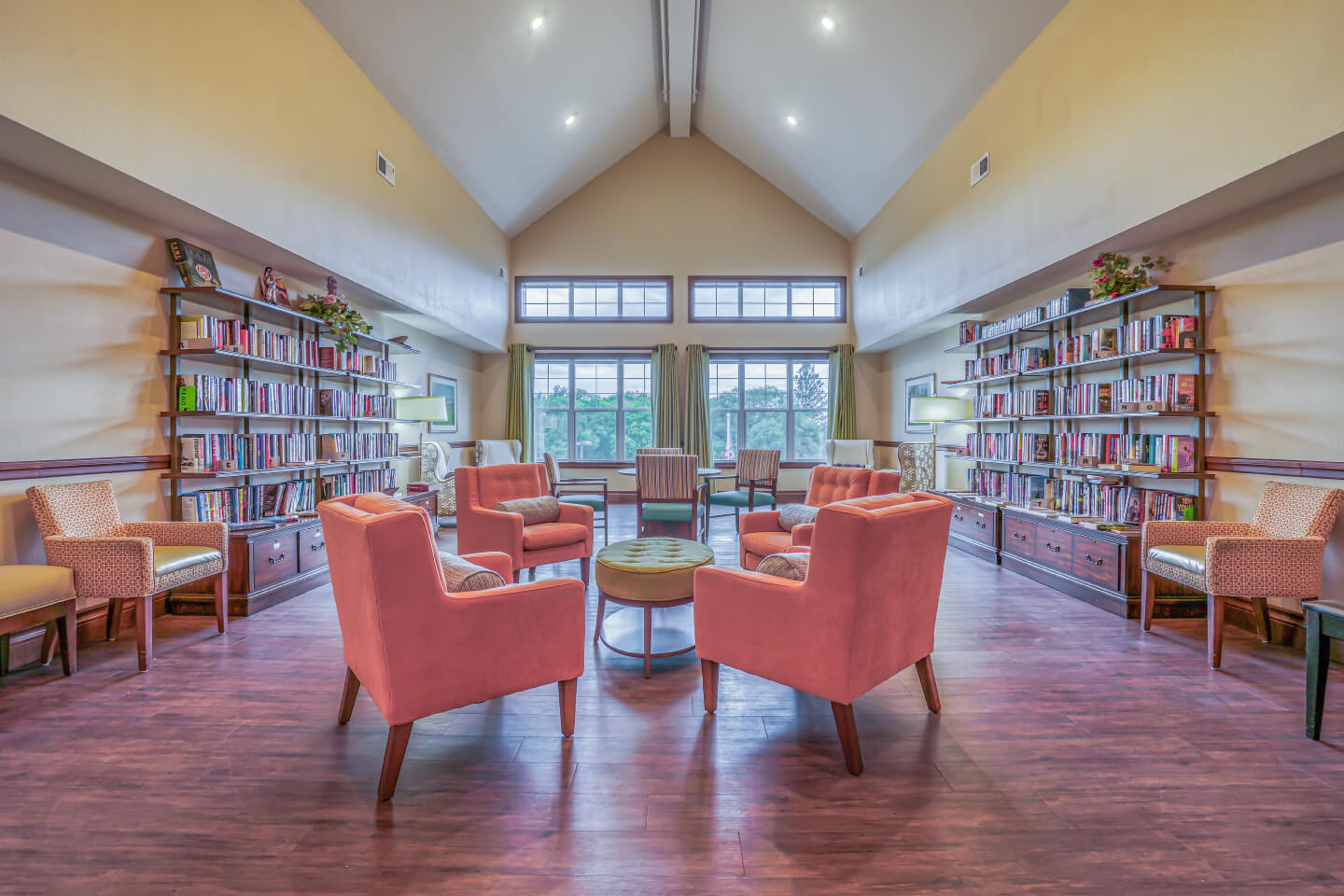 Spacious library area with pink chairs, bookshelves, and large windows in a senior living community.