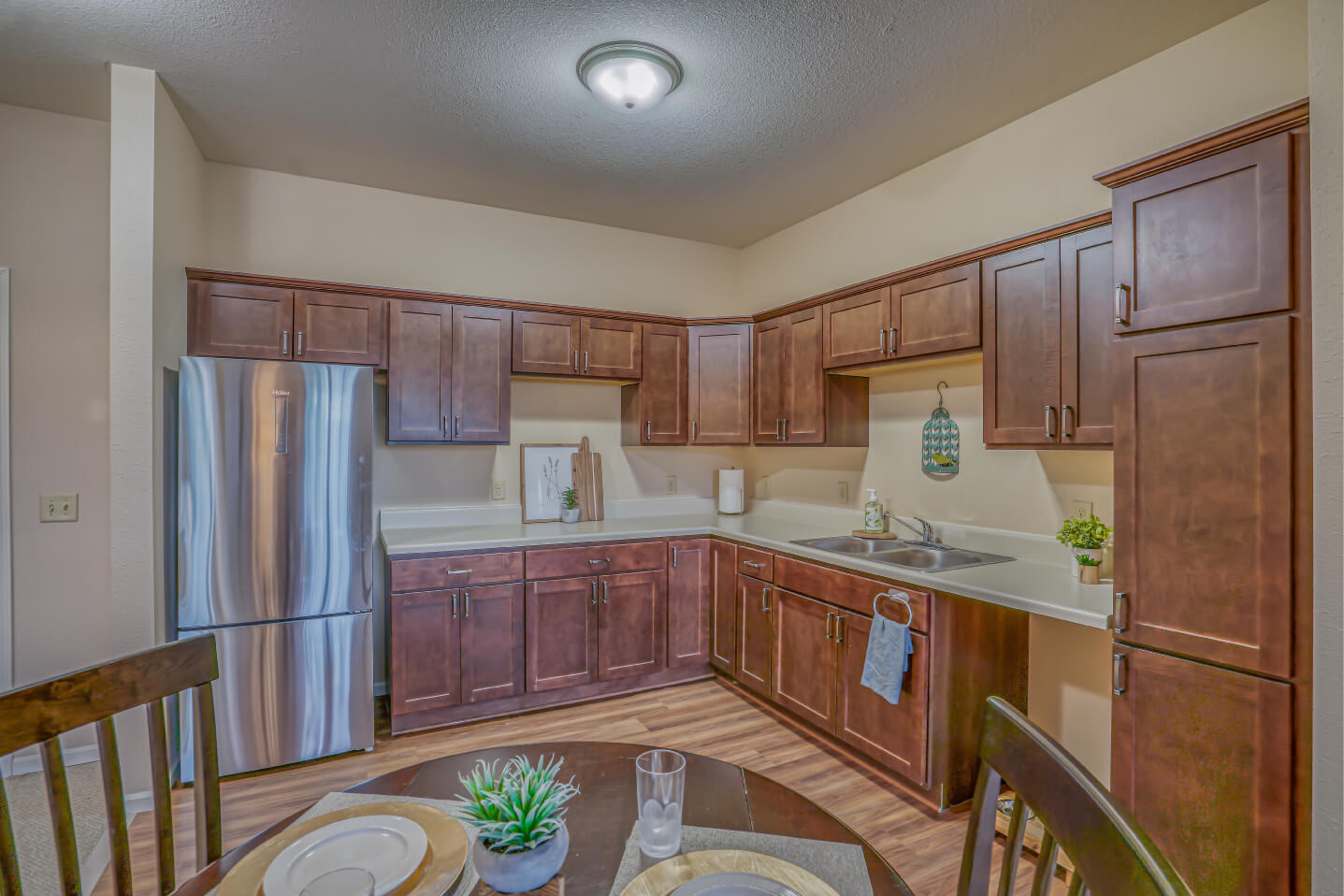 Spacious unit kitchen with brown cabinets, stainless steel appliances, and dining table.