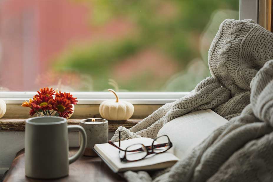 open book with glasses inside in a cozy window nook with a candle burning