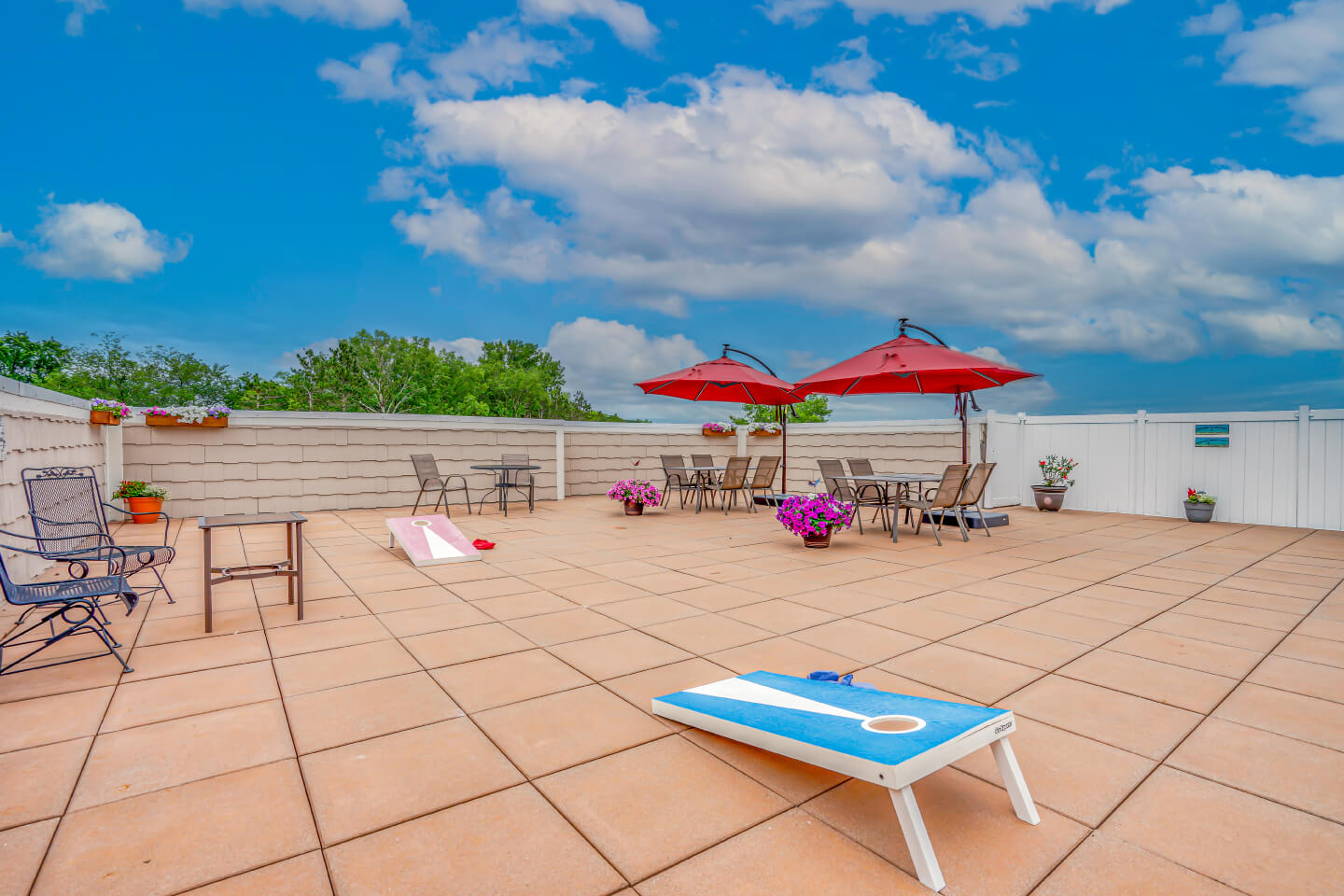 Spacious outdoor patio with seating, red umbrellas, and a cornhole game at a residential community.