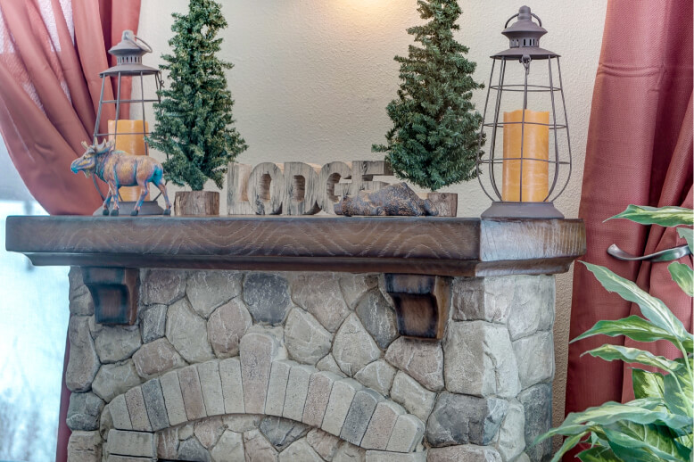 Stone fireplace mantel with rustic lodge-themed decor and lanterns in a cozy memory care unit.