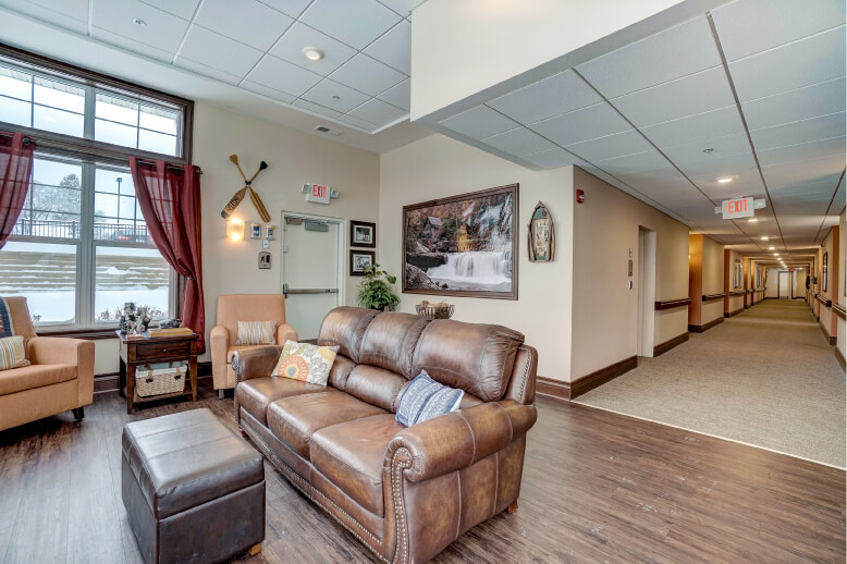 Comfortable seating area with leather couches and armchairs in a memory care facility hallway.