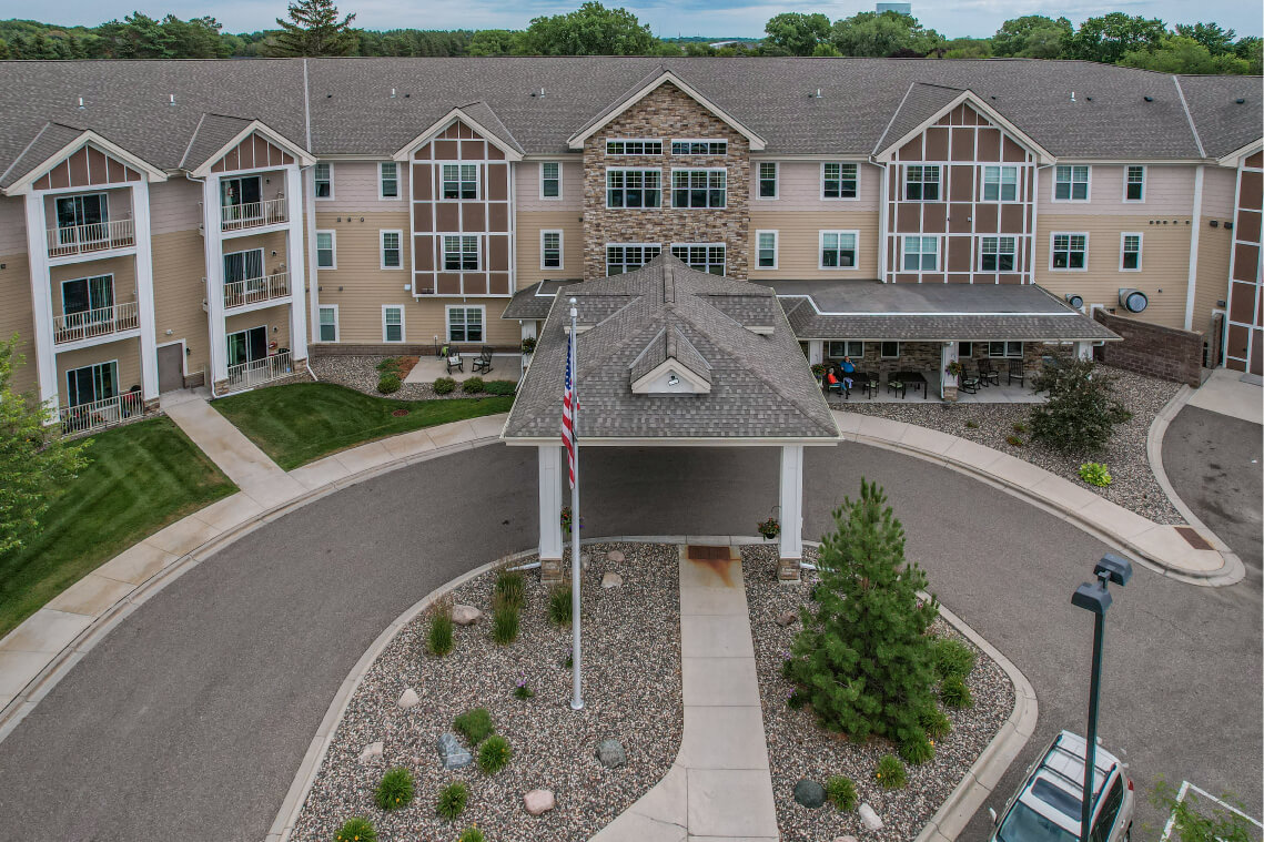 Aerial view of a senior living community with flagpole at entrance and landscaped roundabout.