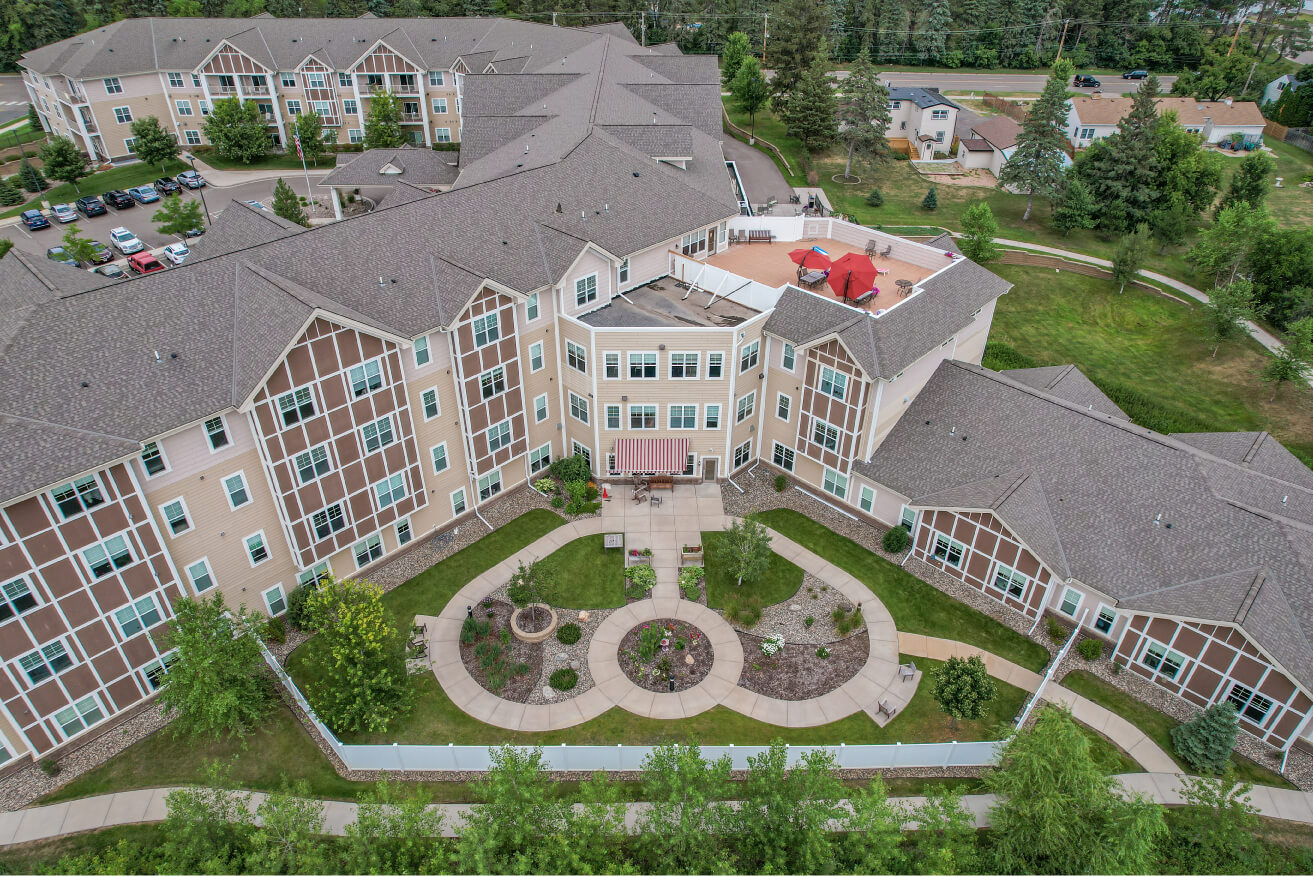 Birds eye view of a large senior living community with landscaped garden paths and parking lot.