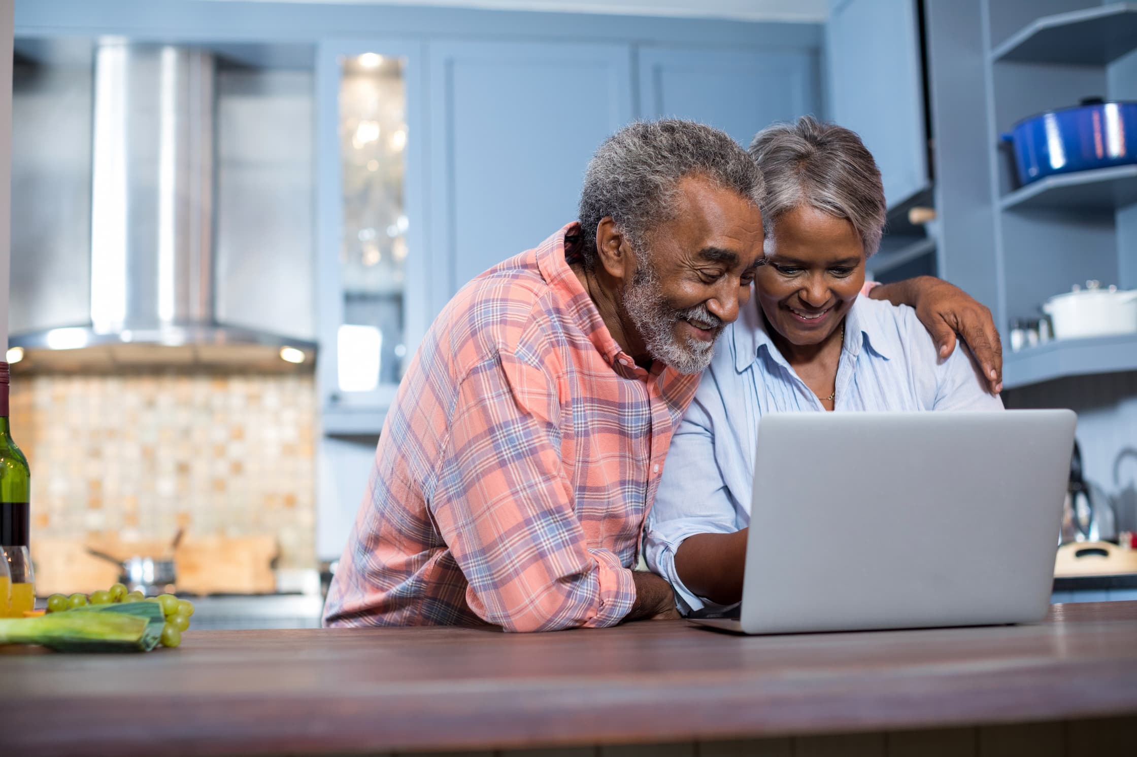 senior couple smiles at laptop in their kitchen
